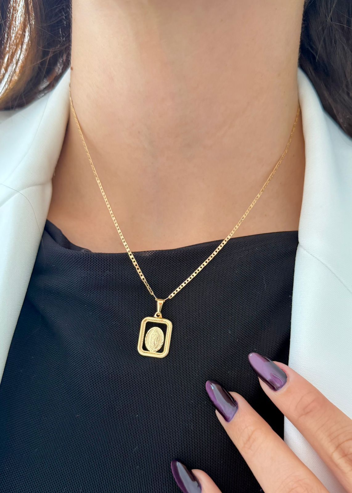 Un collar de oro con un colgante de marco rectangular que luce un pequeño emblema ovalado