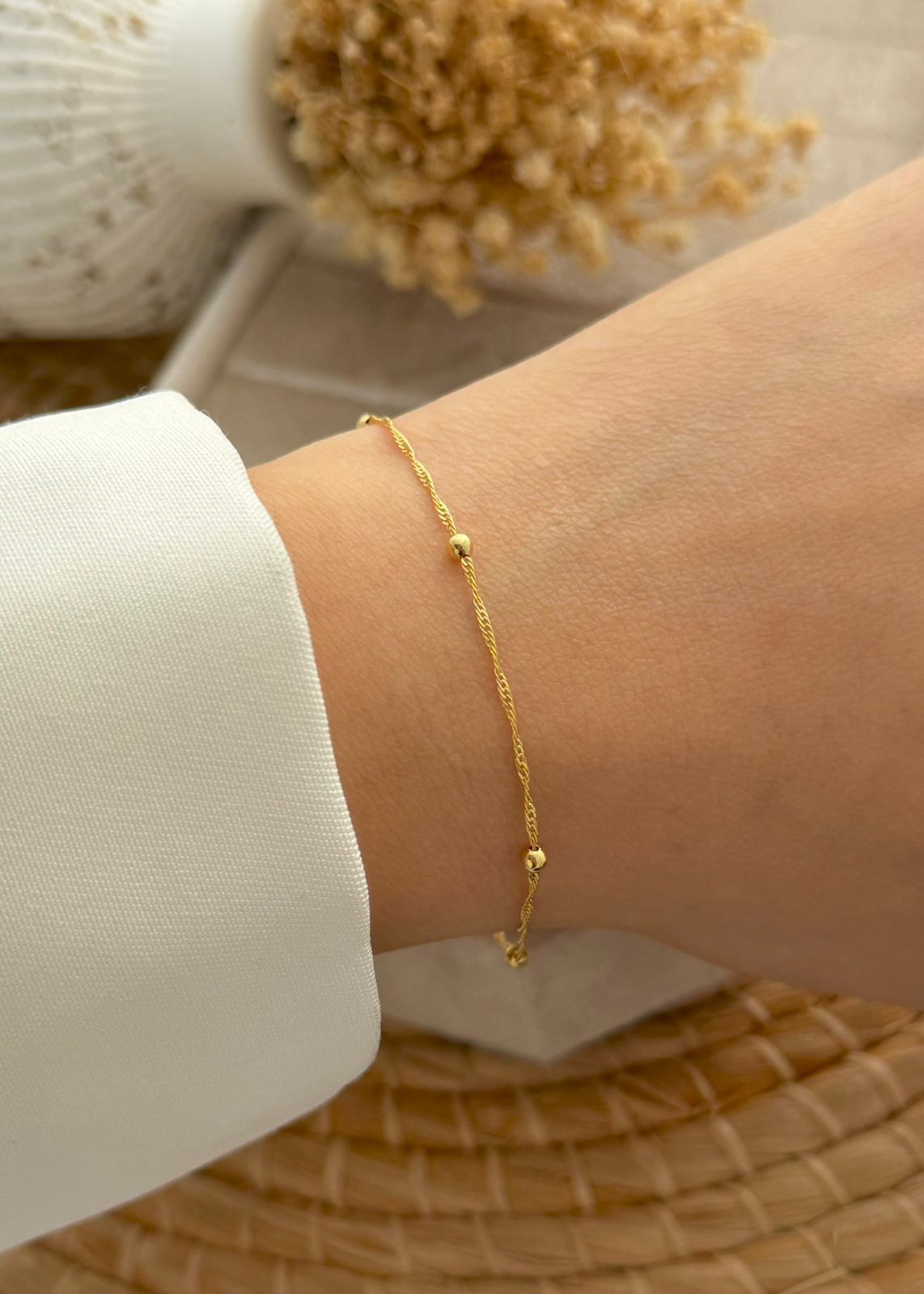 Una pulsera de cadena fina y delicada de oro con pequeñas cuentas de oro espaciadas uniformemente en la muñeca