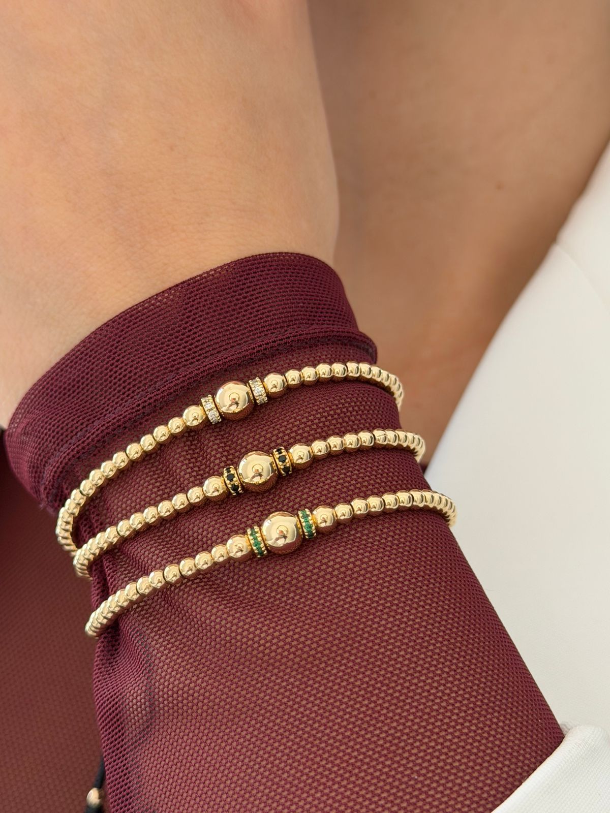 Tres pulseras elásticas de cuentas doradas en una muñeca, cada una con una bola dorada central 