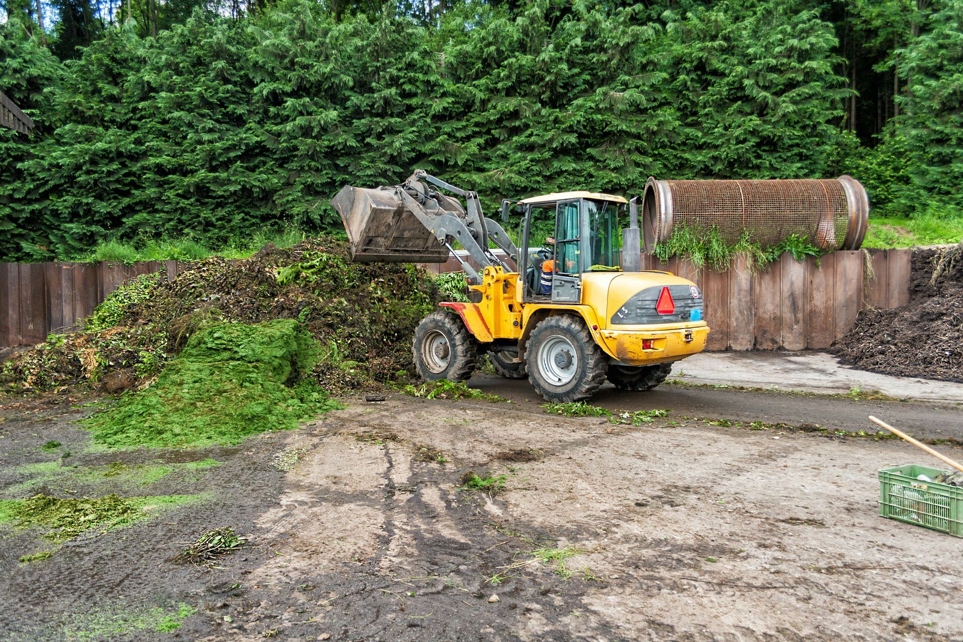 A yellow bulldozer is loading a pile of grass in a dirt field.