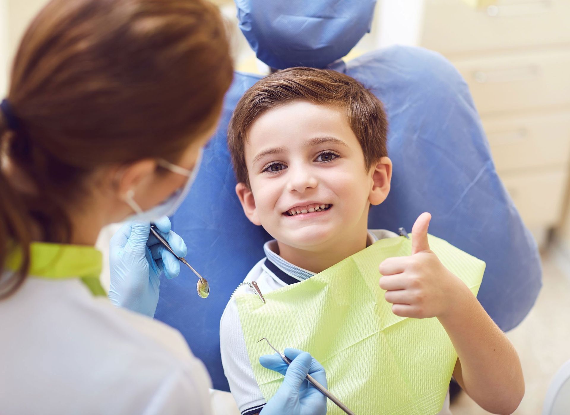 A young boy is giving a thumbs up while sitting in a dental chair.