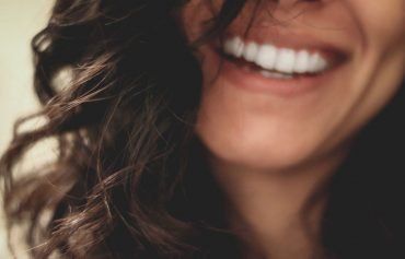 A close up of a woman 's face smiling with her hair blowing in the wind.