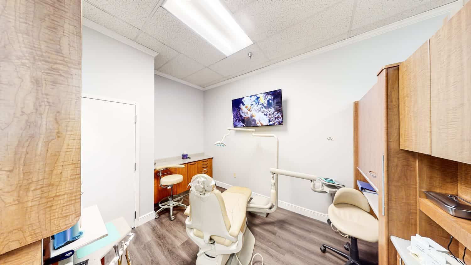 A dental office with a dental chair and a television on the wall.