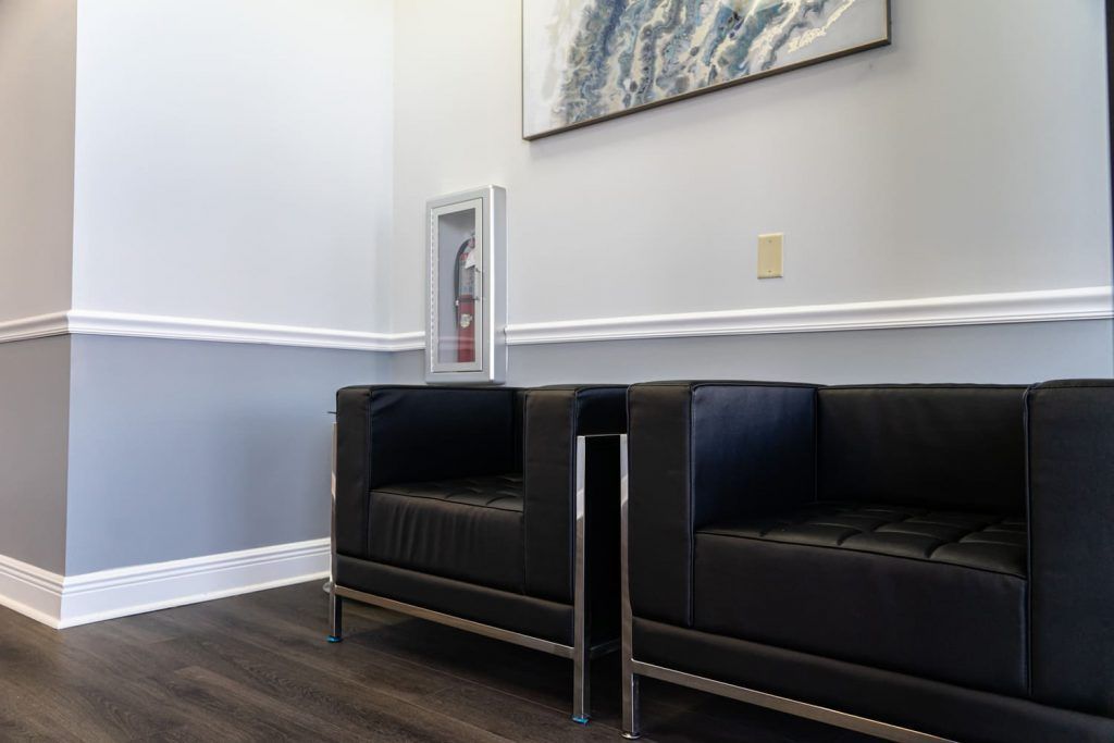A waiting room with two black leather couches and a painting on the wall.