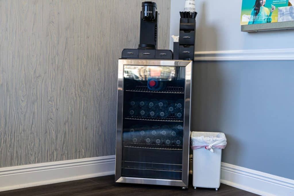 A small refrigerator is sitting in a corner of a room next to a trash can.