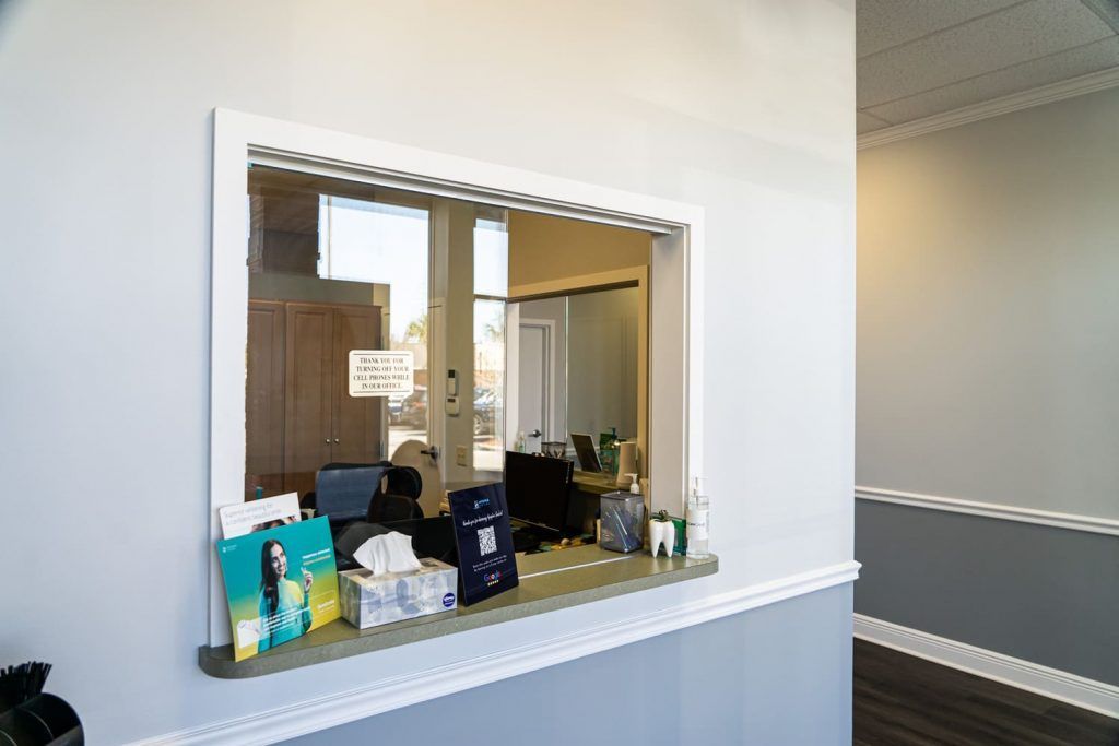 There is a window in the wall in the reception area of a dental office.