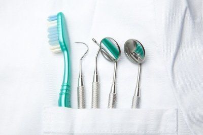 A toothbrush , dental mirrors , and dental instruments are in a pocket of a dentist 's coat.