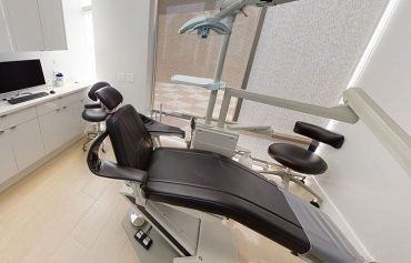 A dental office with a black dental chair and a computer.
