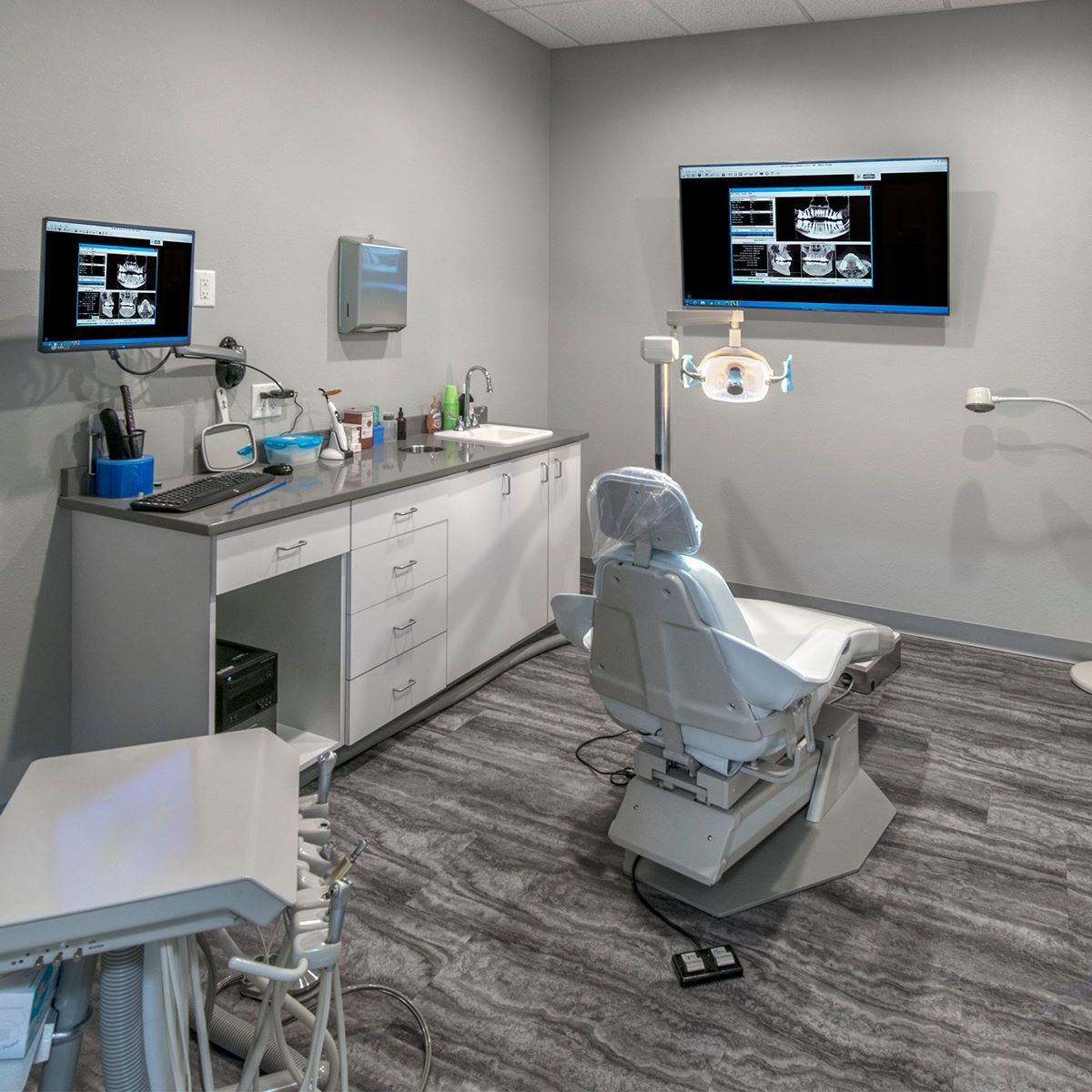 A dental office with a dental chair and two monitors