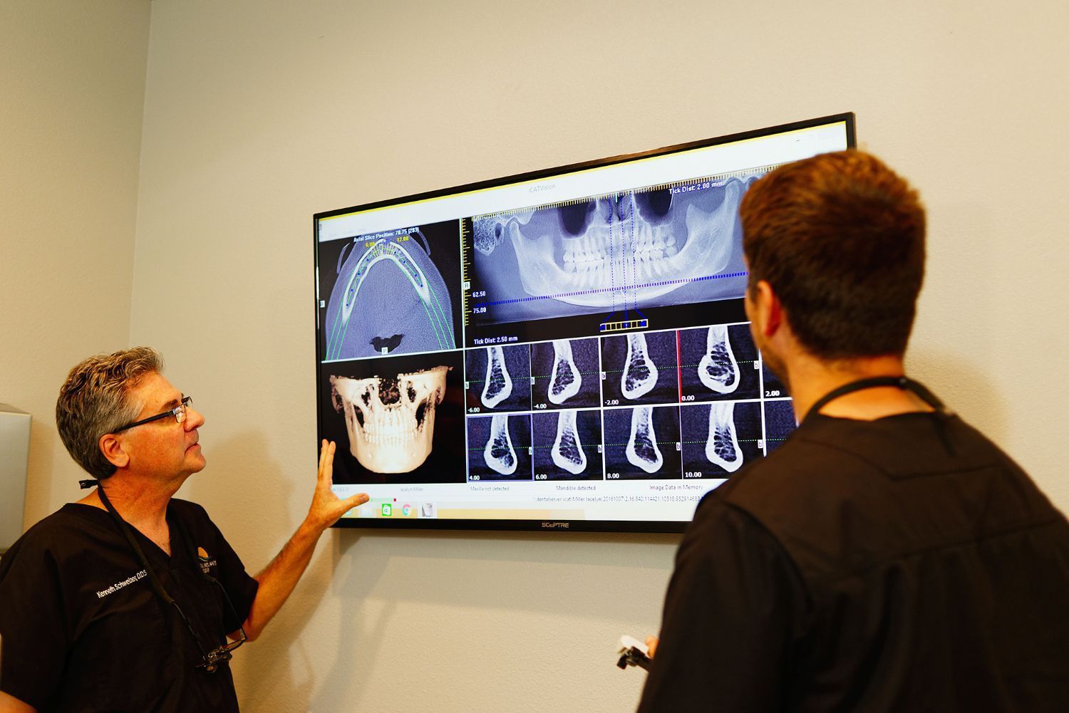 Two men are looking at an x-ray of a skull on a television screen.