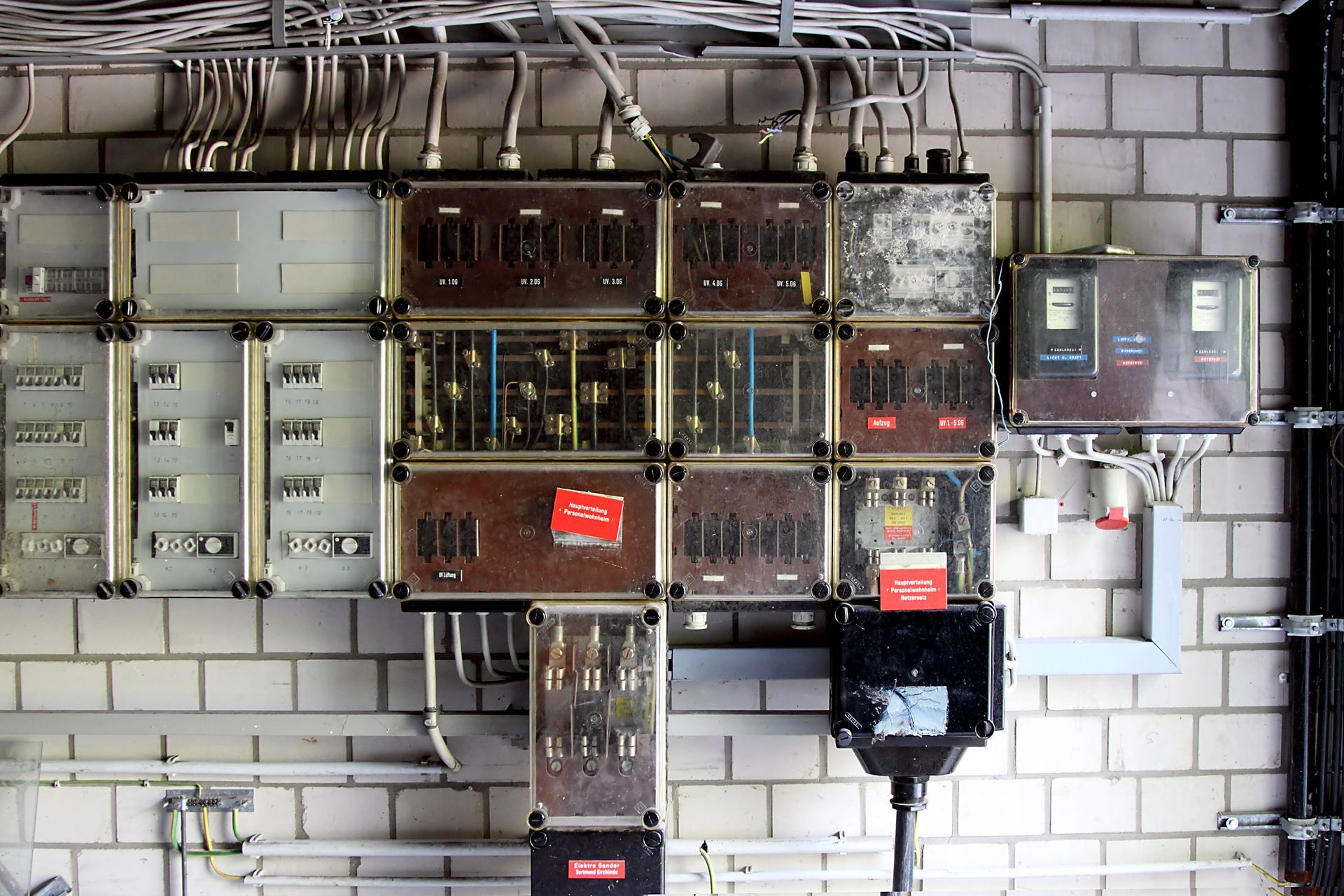 Elektrische Schaltschränke an einer weißen Backsteinwand, darüber verlaufen Kabel und Leitungen.