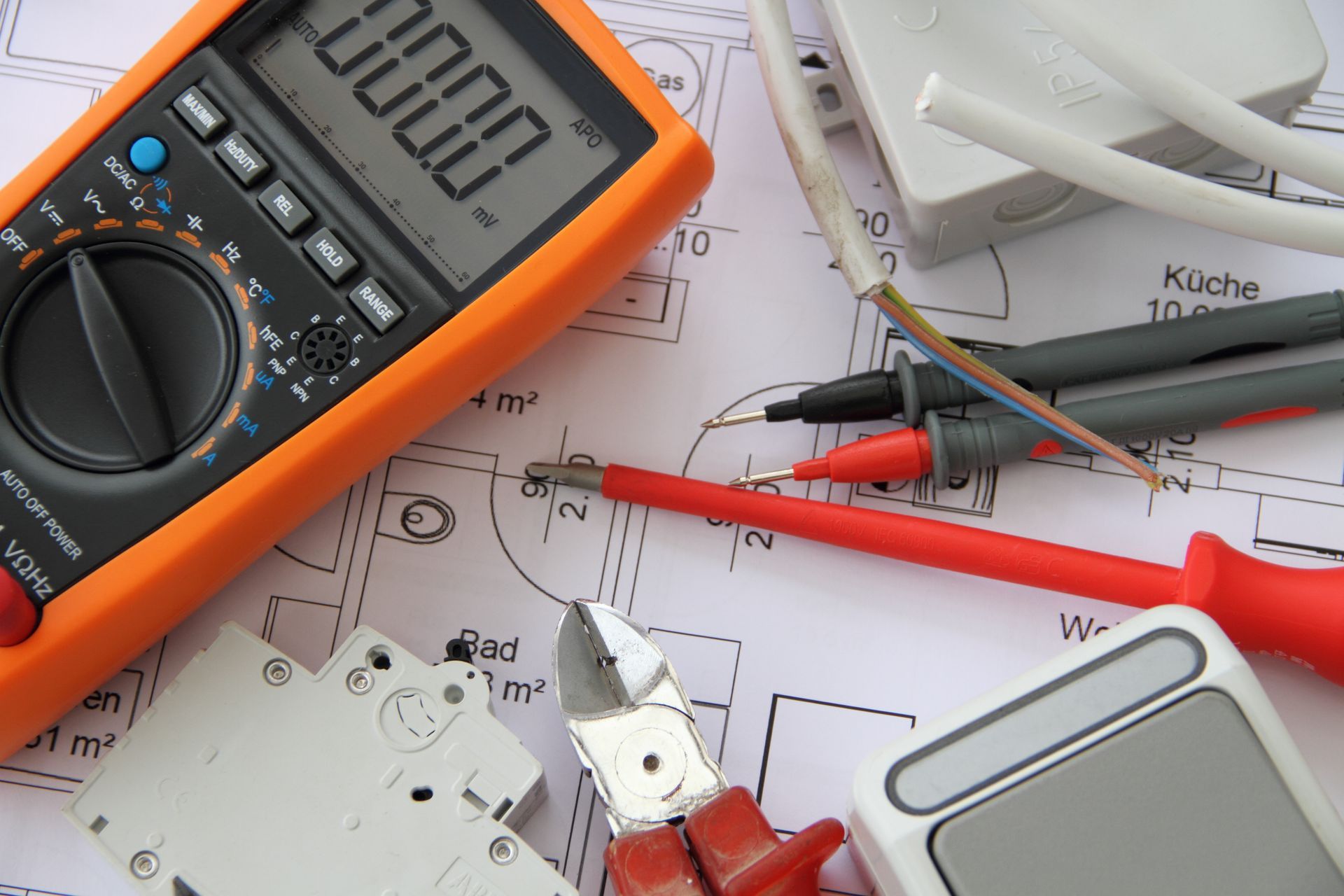 Ein orangefarbenes Multimeter, Elektrowerkzeuge und Kabel auf einem Bauplan.
