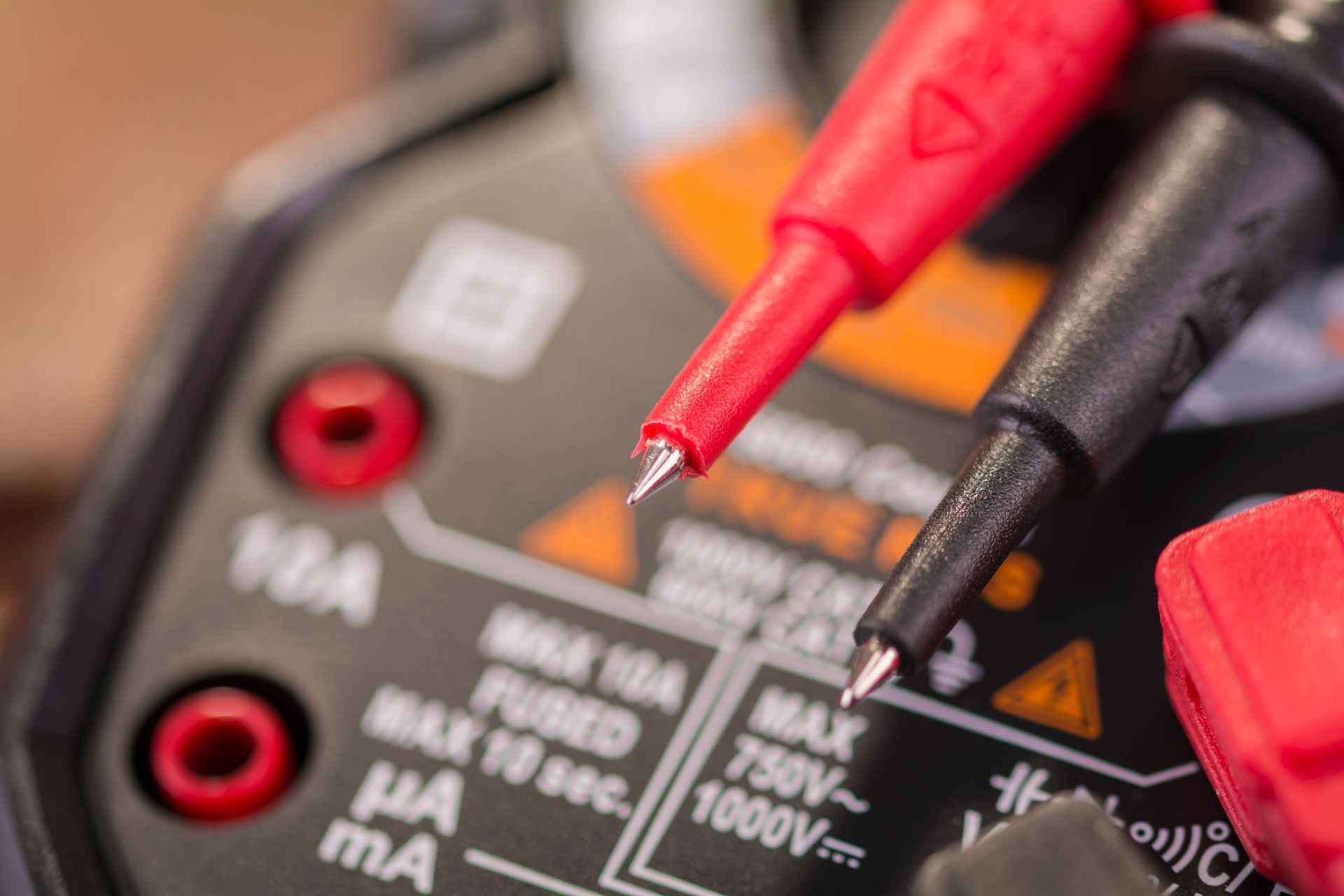 Rote und schwarze Multimeterspitzen an einem schwarzen Messgerät mit orangefarbenen und weißen Markierungen; Nahaufnahme.