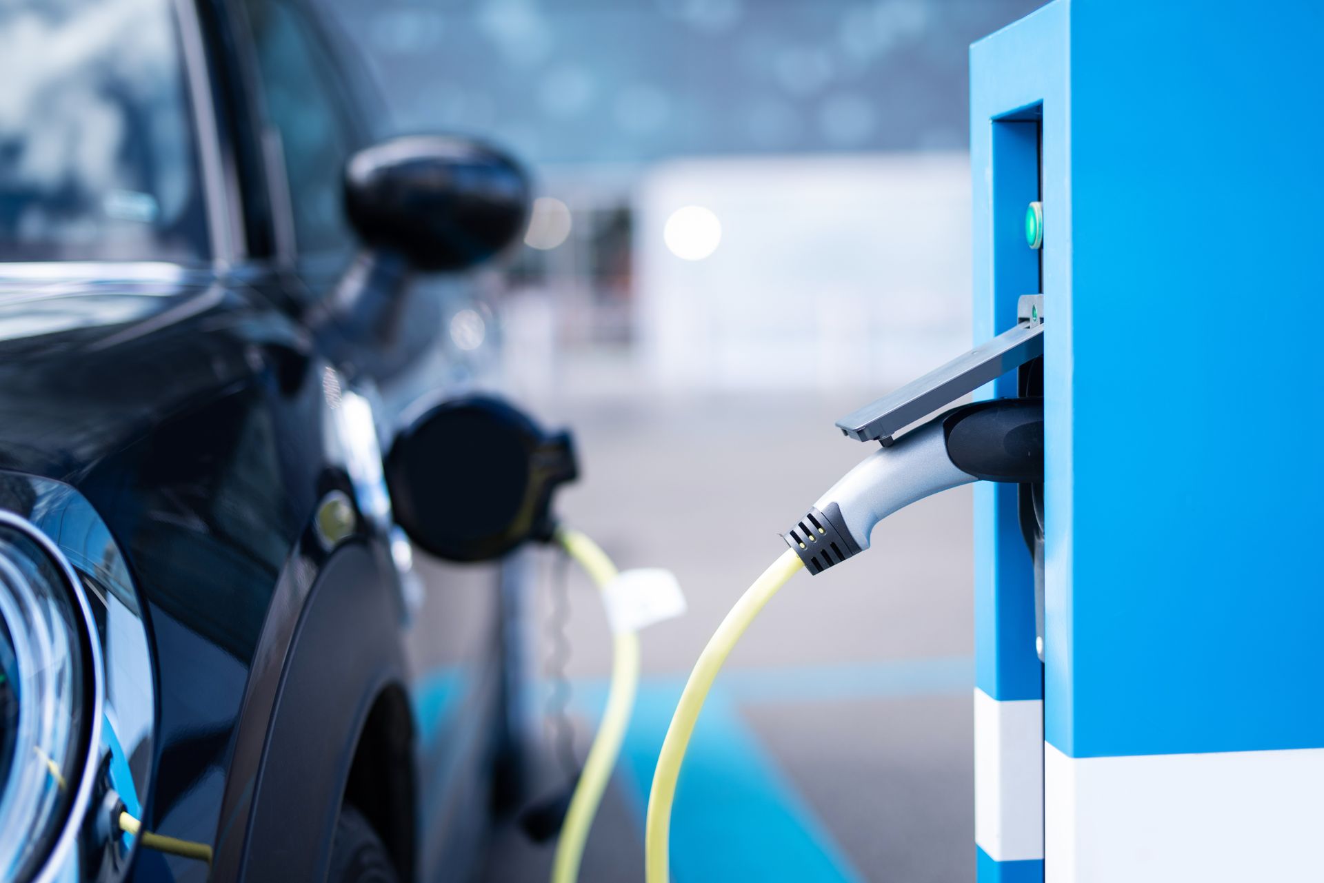 Schwarzes Elektroauto lädt an einer blauen Ladestation.