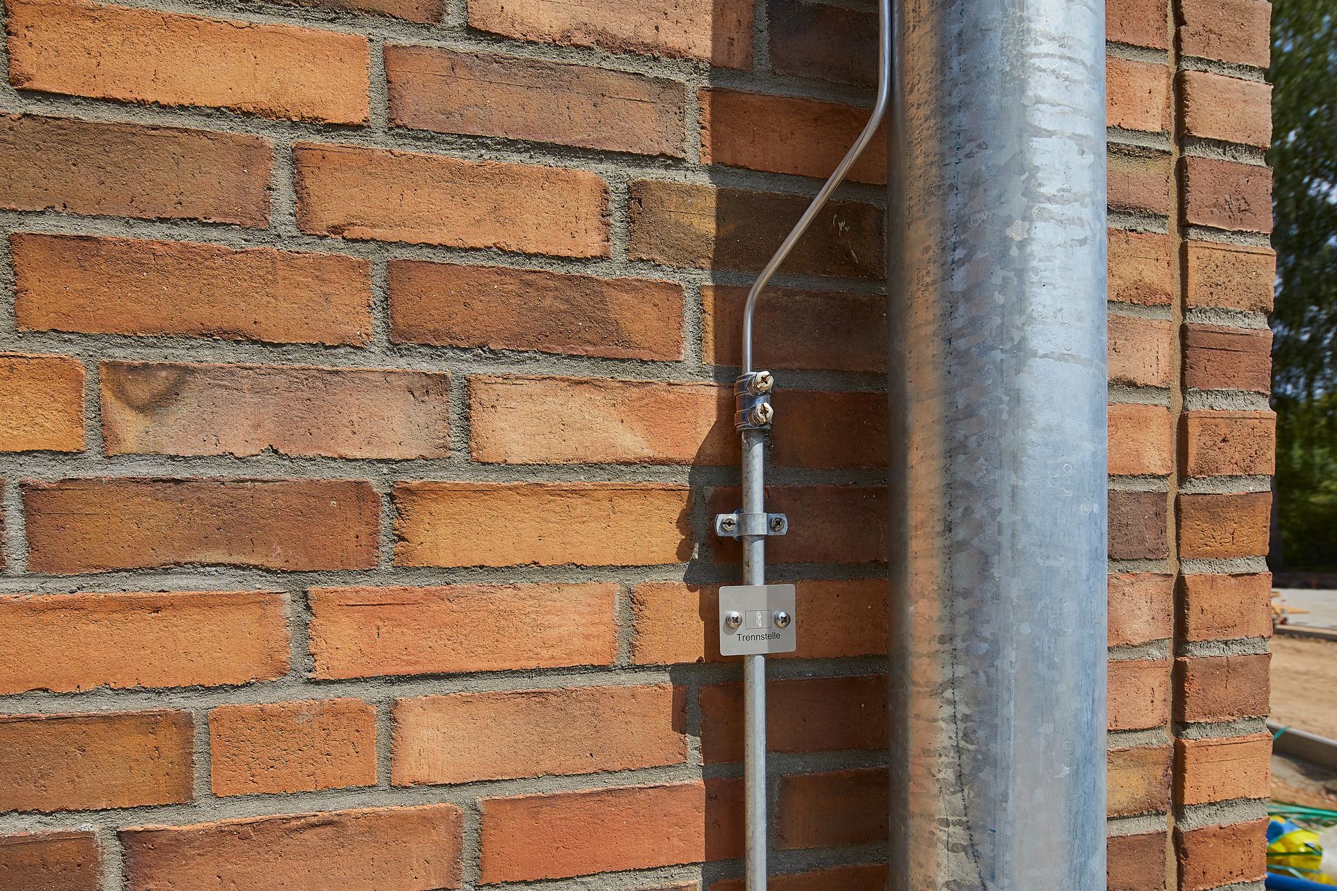 Ein an einer Ziegelwand neben einem Metallmast befestigtes elektrisches Metallrohr.