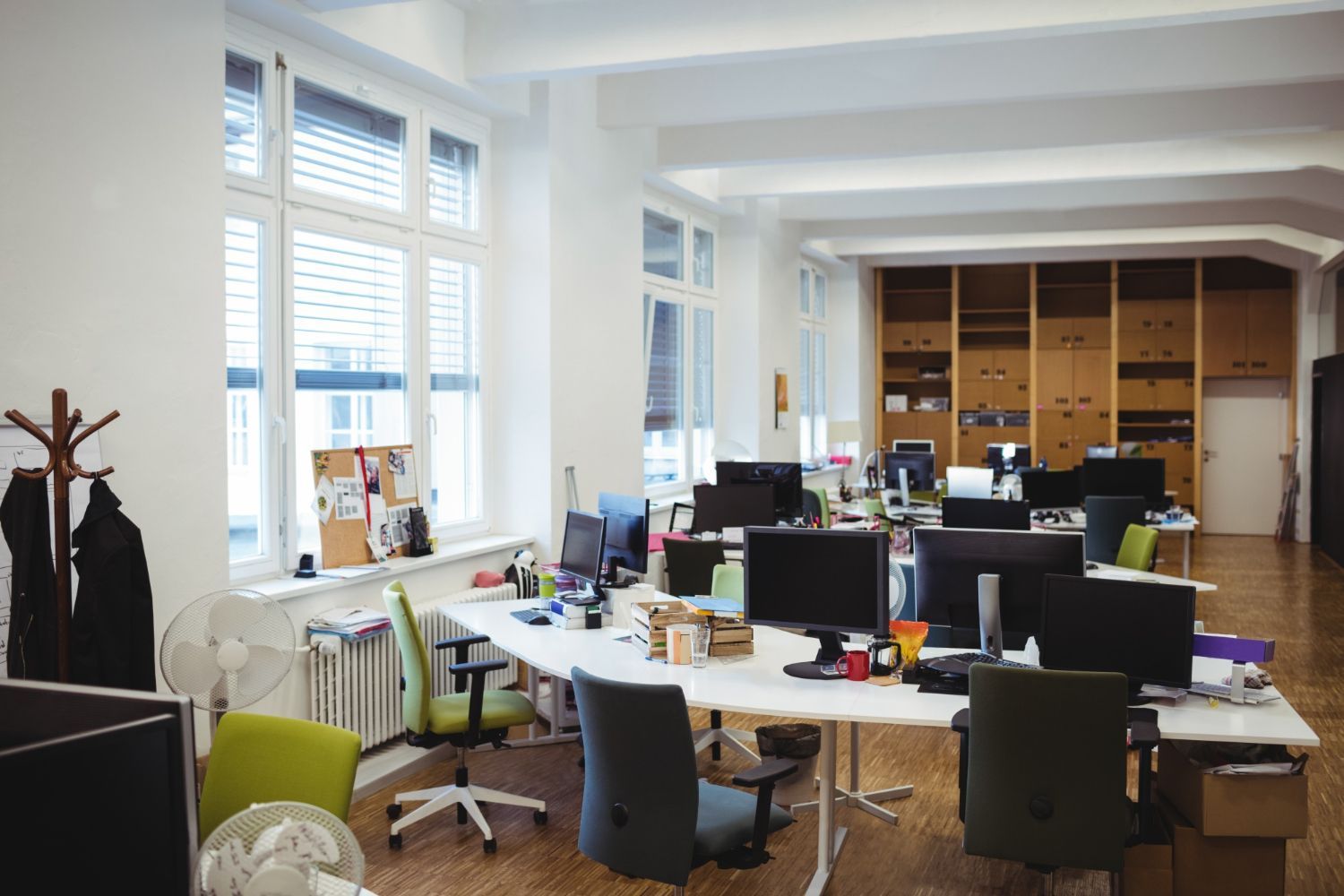 Modern office with desks, computers, chairs, and large windows along the left wall