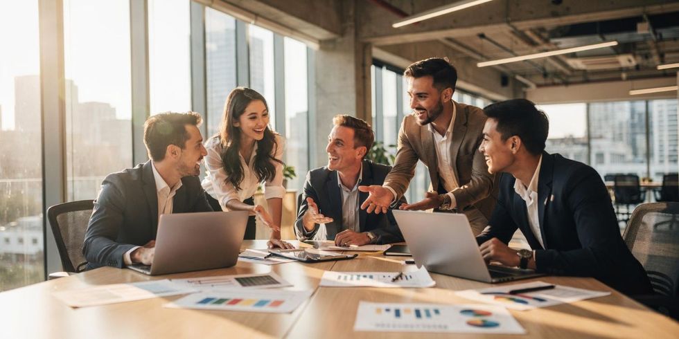 Business team in a meeting around a table in a sunlit office, discussing documents and laptops