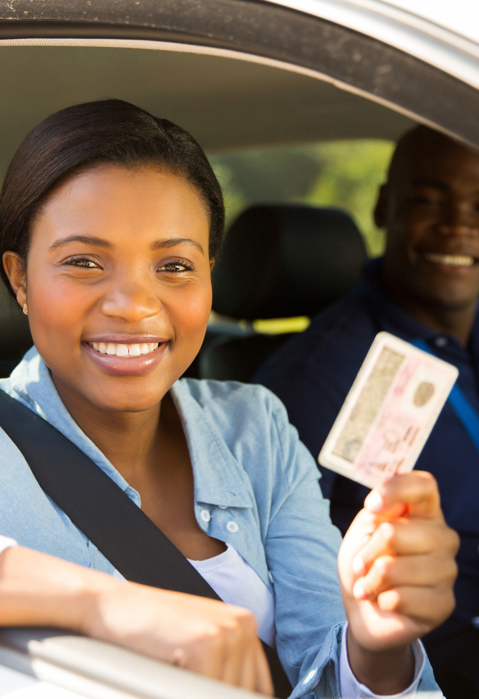 A woman is sitting in a car holding a driving license.