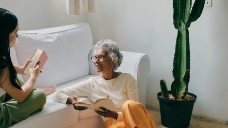 Two women are sitting on a couch reading books.