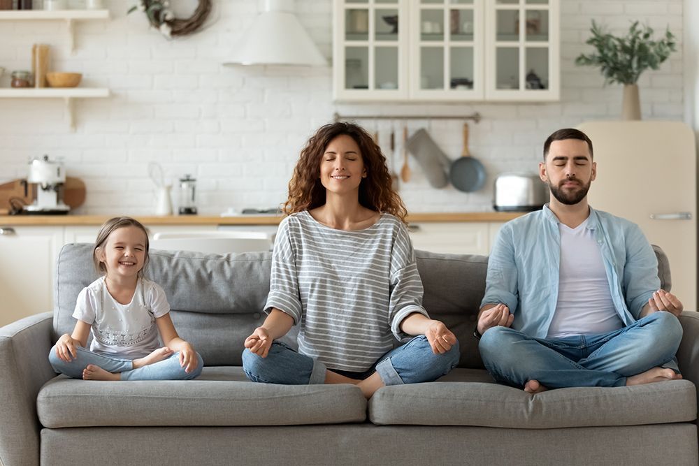 A family is meditating on a couch in a living room.