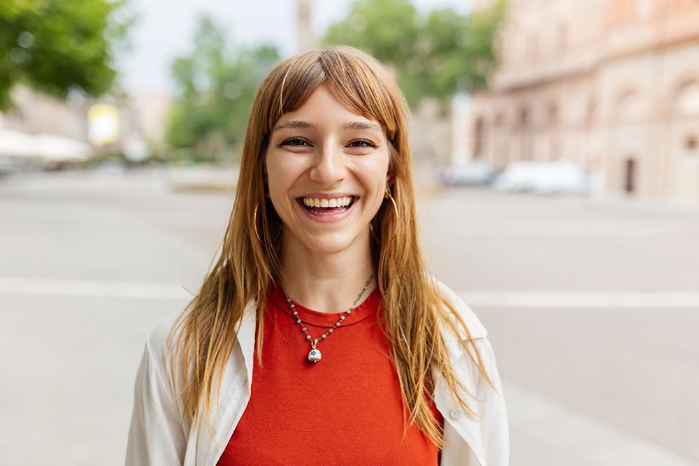 A young woman is smiling while standing on a sidewalk in the city.