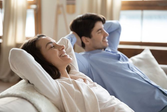 A man and a woman are sitting on a couch with their arms behind their head.