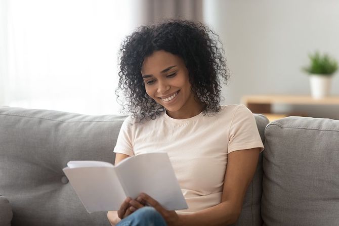 A woman is sitting on a couch reading a book.