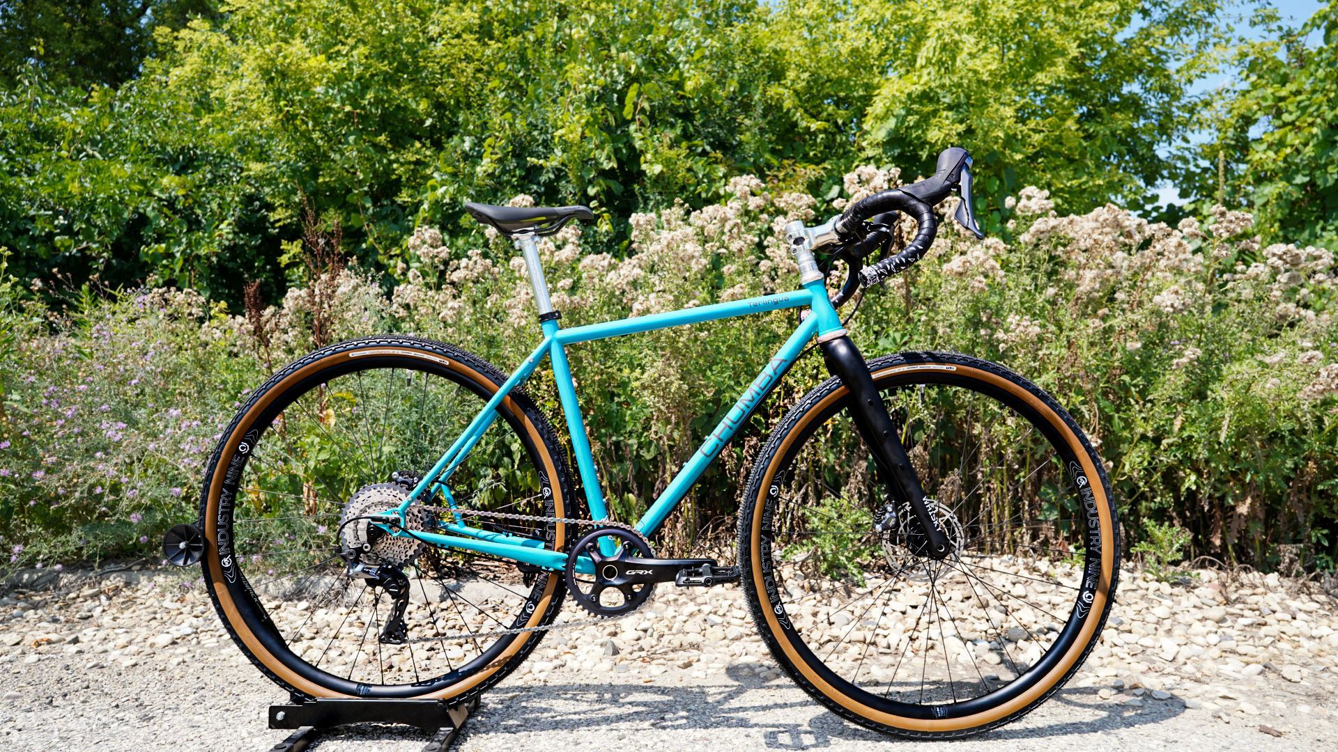 A blue bicycle is parked on a gravel road in front of trees.