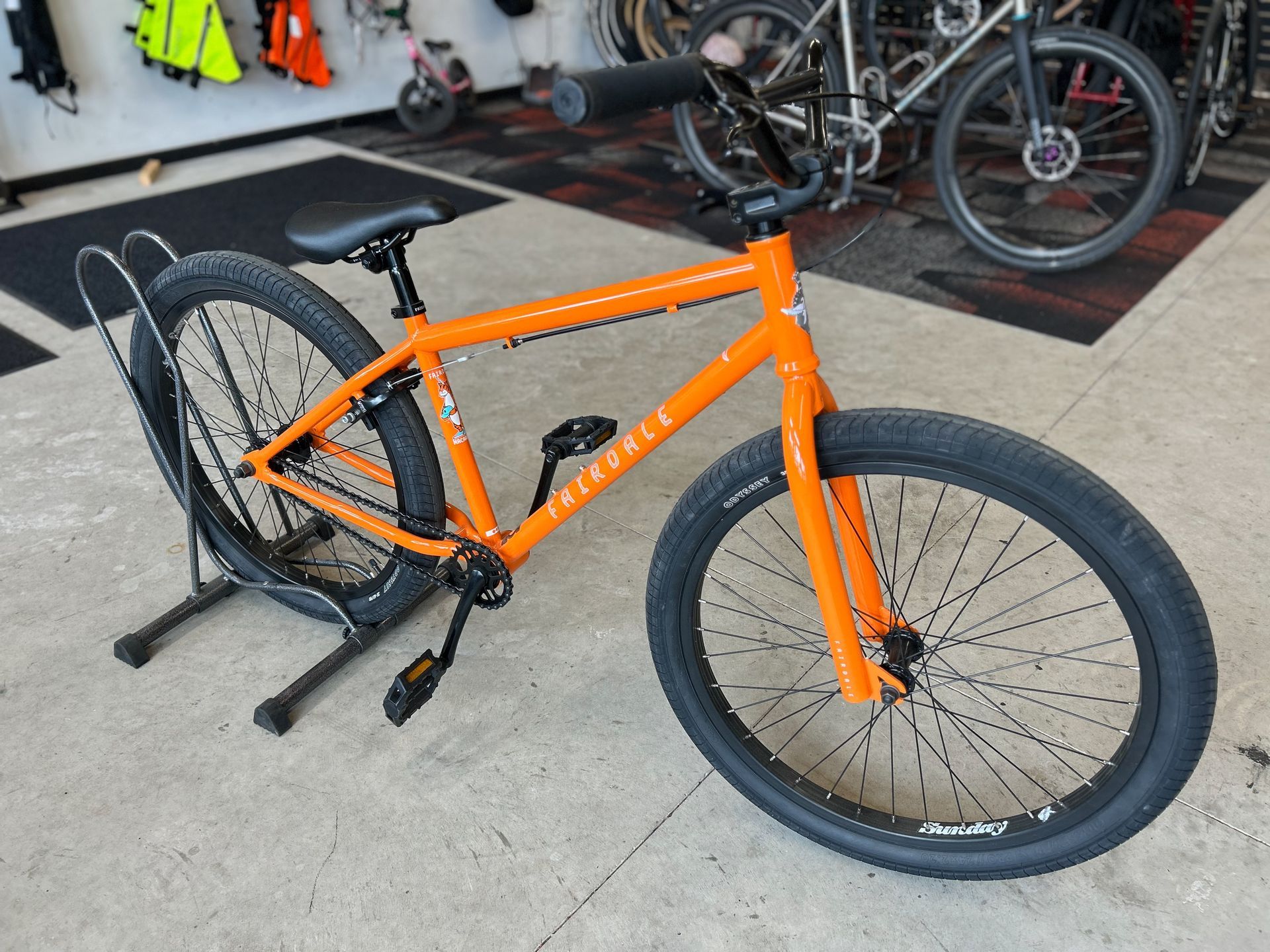 An orange bicycle is parked on a rack in a store.