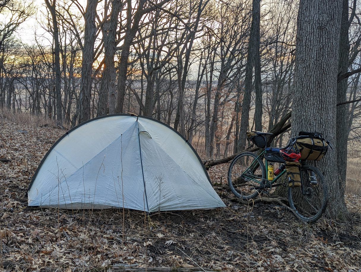 A tent is sitting next to a bicycle in the woods.