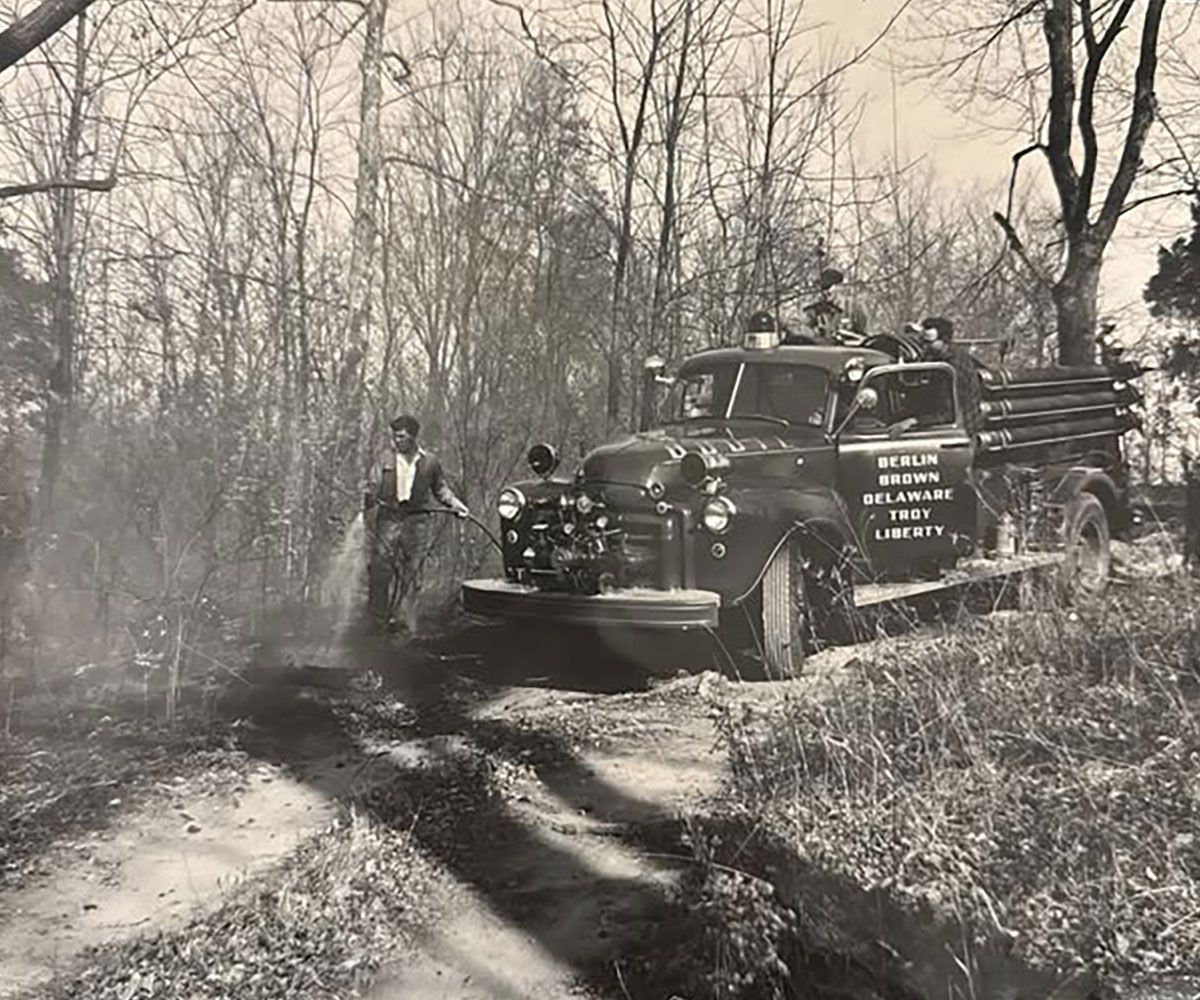 Tri Township black and white historical photo of original fire engine with man holding hose near it circa late 1940s