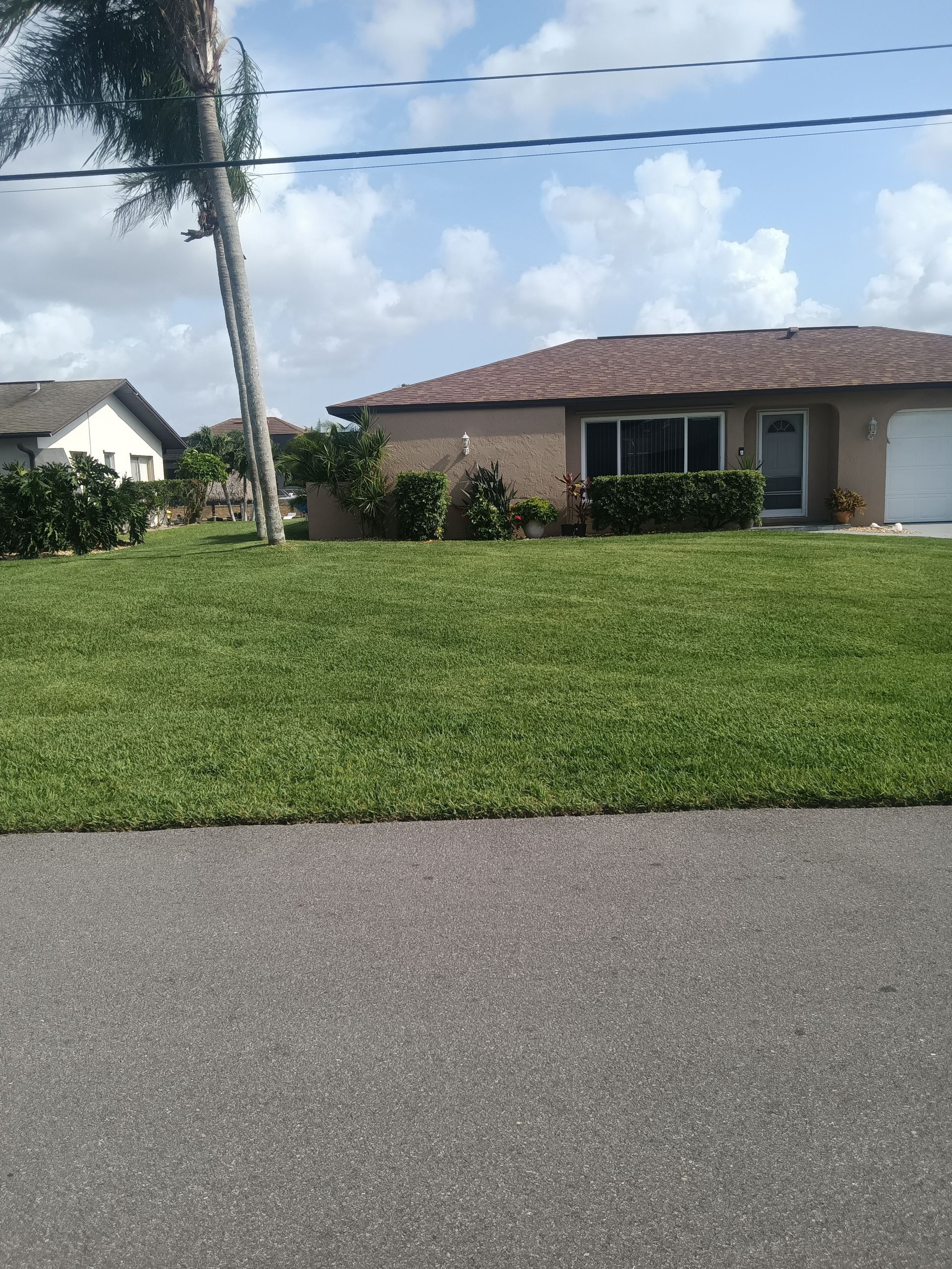 Tan house with red tile roof and well-manicured lawn on a sunny day.
