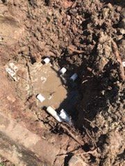 Hole in the ground filled with water and white pipes, surrounded by dirt.