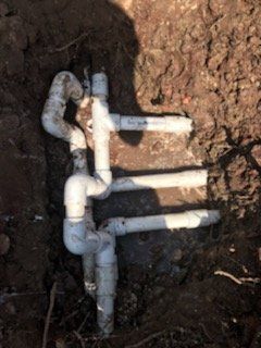 White PVC pipes in a dirt trench, appearing to be plumbing or irrigation system components.