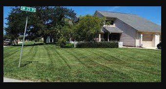 Lawn with fresh mowing stripes, street sign, house with garage. Green grass, blue sky.
