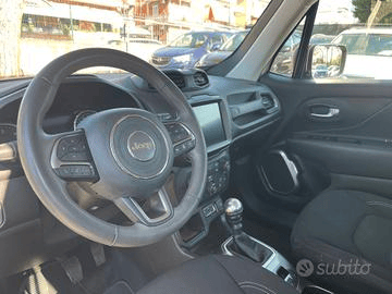 Cruscotto di un'auto con lo schermo di navigazione che mostra una visuale della telecamera posteriore e una vista dall'alto dell'auto, circondata da pulsanti e comandi del climatizzatore.