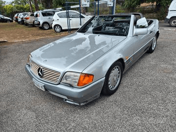 Mercedes-Benz decappottabile color argento parcheggiata in un parcheggio, con capote abbassata. Vista frontale, con la decorazione sul cofano e uno scorcio degli interni.