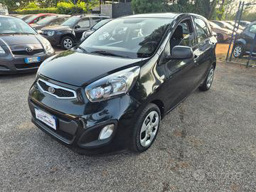 Kia Picanto nera parcheggiata su un piazzale ghiaioso, alla luce del sole. Sullo sfondo si vedono altri veicoli.