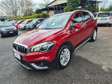 Un SUV Suzuki S-Cross rosso parcheggiato in un parcheggio in una giornata di sole, circondato da altri veicoli.