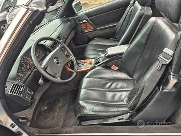 Vista interna di una classica Mercedes-Benz decappottabile. Sono visibili i sedili in pelle nera, gli inserti in legno e il cruscotto; l'auto è parcheggiata all'aperto.