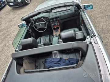 Vista interna di una Mercedes-Benz decappottabile color argento con sedili in pelle nera, capote abbassata. Il cruscotto è visibile.