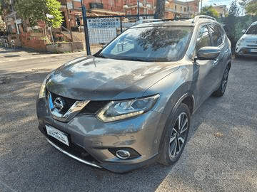 Un SUV Nissan X-Trail grigio parcheggiato in una strada cittadina. L'auto è rivolta verso la telecamera; altre auto ed edifici sono sullo sfondo.
