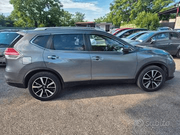 Nissan X-Trail grigia parcheggiata su un piazzale asfaltato insieme ad altri veicoli. Ripresa diurna.