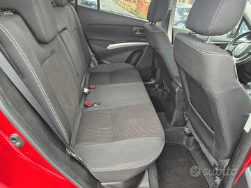 Interno posteriore di un'auto rossa con sedili in tessuto nero, cuciture bianche e cinture di sicurezza.