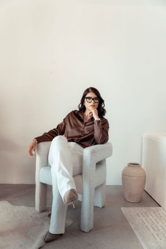 A woman is sitting at a desk with a laptop and a vase of flowers.
