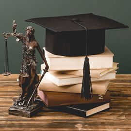 A statue of lady justice standing next to a stack of books and a graduation cap