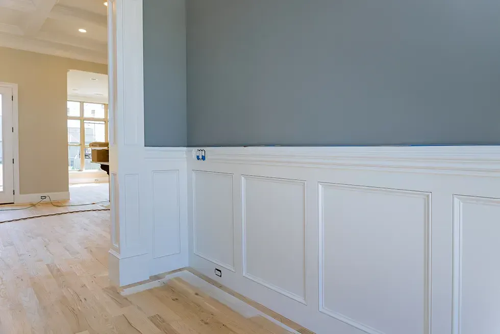 A corner of a room with white paneling and a gray wall.