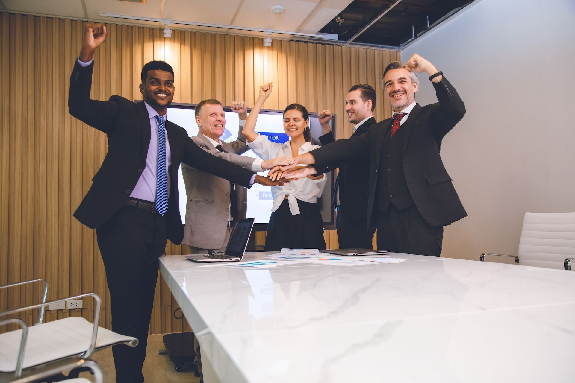 A group of business people are putting their hands together in a conference room.