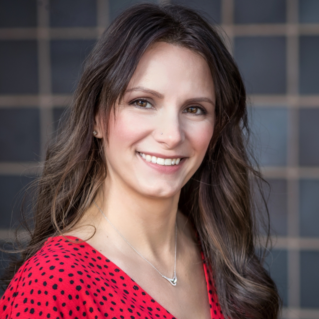 A woman wearing a red polka dot shirt and a necklace smiles for the camera.