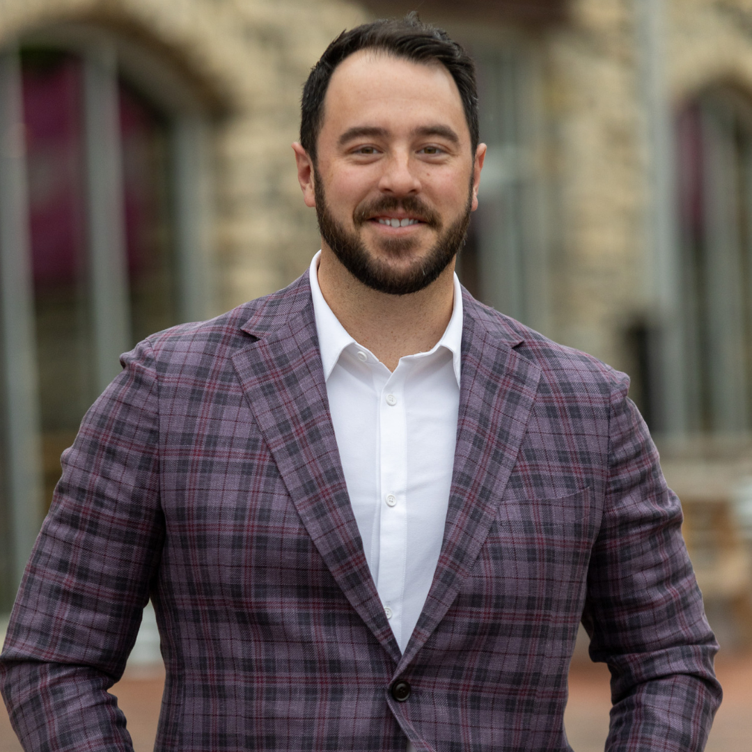 A man with a beard is wearing a plaid jacket and a white shirt.